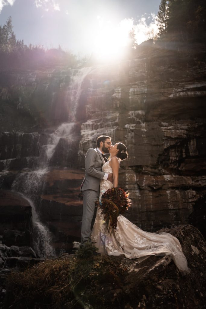 Beautiful wedding photo of Bride and Groom kissing on a majestic mountain rocks waterfall with natural lighting