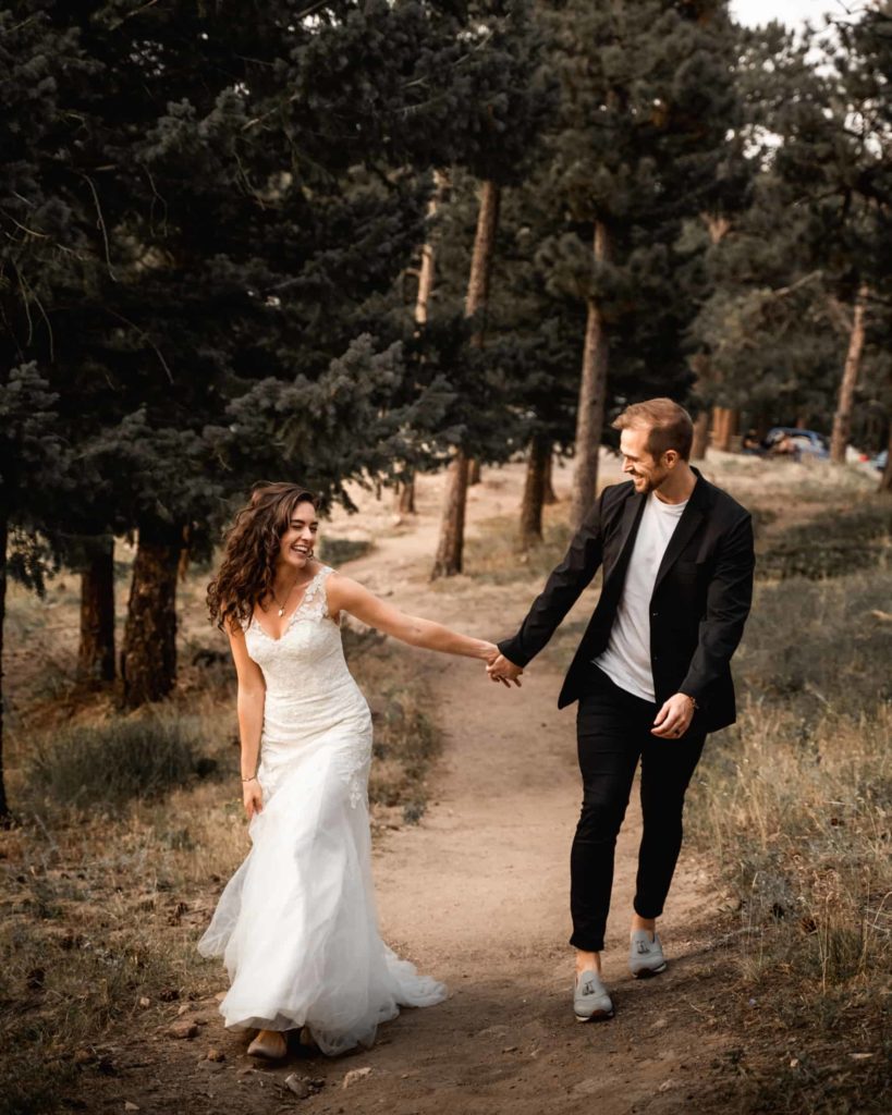 Wedding photo of Bride and Groom playfully walking down a forest path holding hands happily