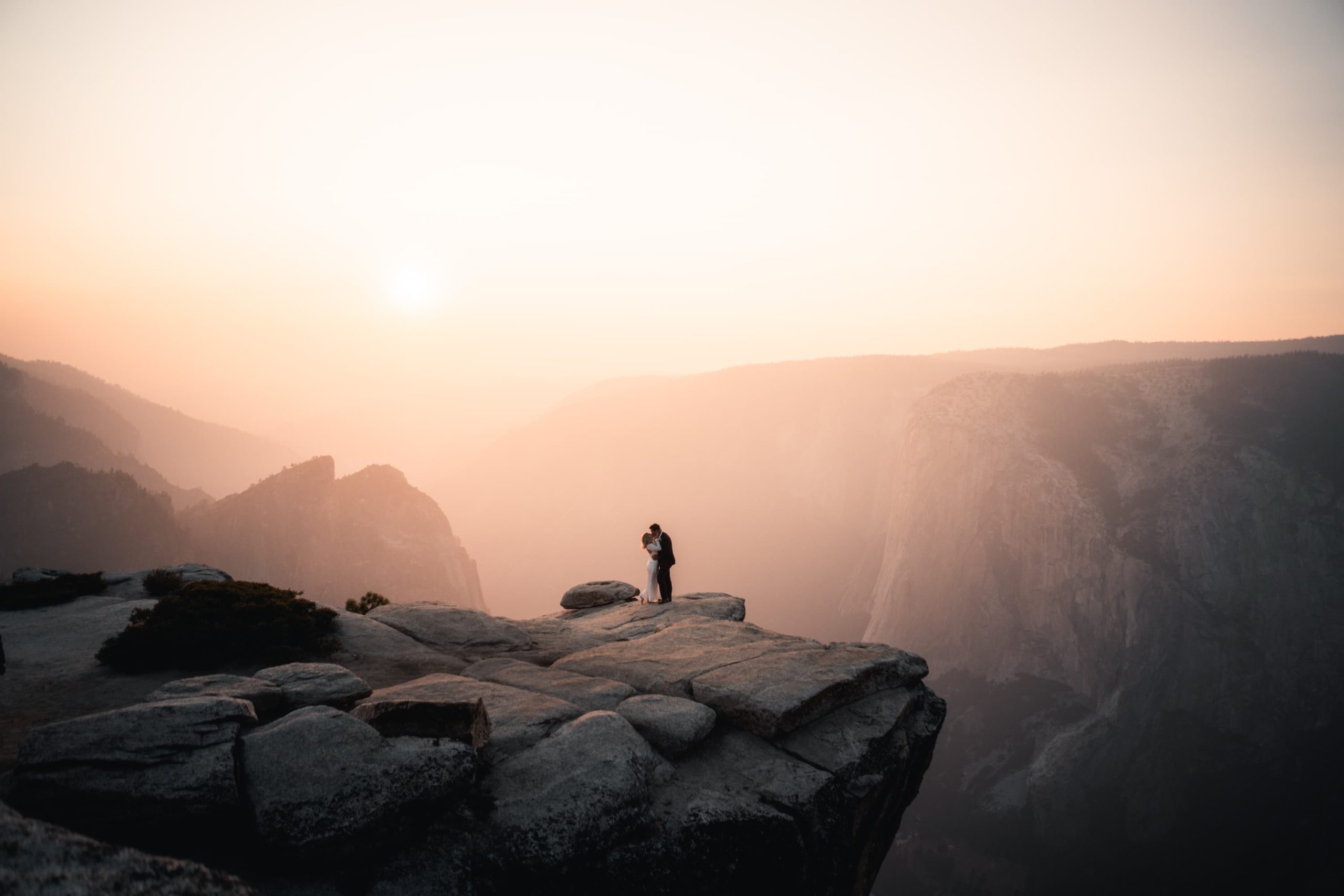 adventure elopement photo of Breath taking wedding photo of Bride and Groom kissing on a cliffside rock formation along the mountain ranges with amazing sunset