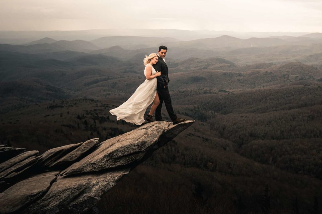 Wedding photo of Bride and Groom on cliffside rock with amazing view of hills and mountains