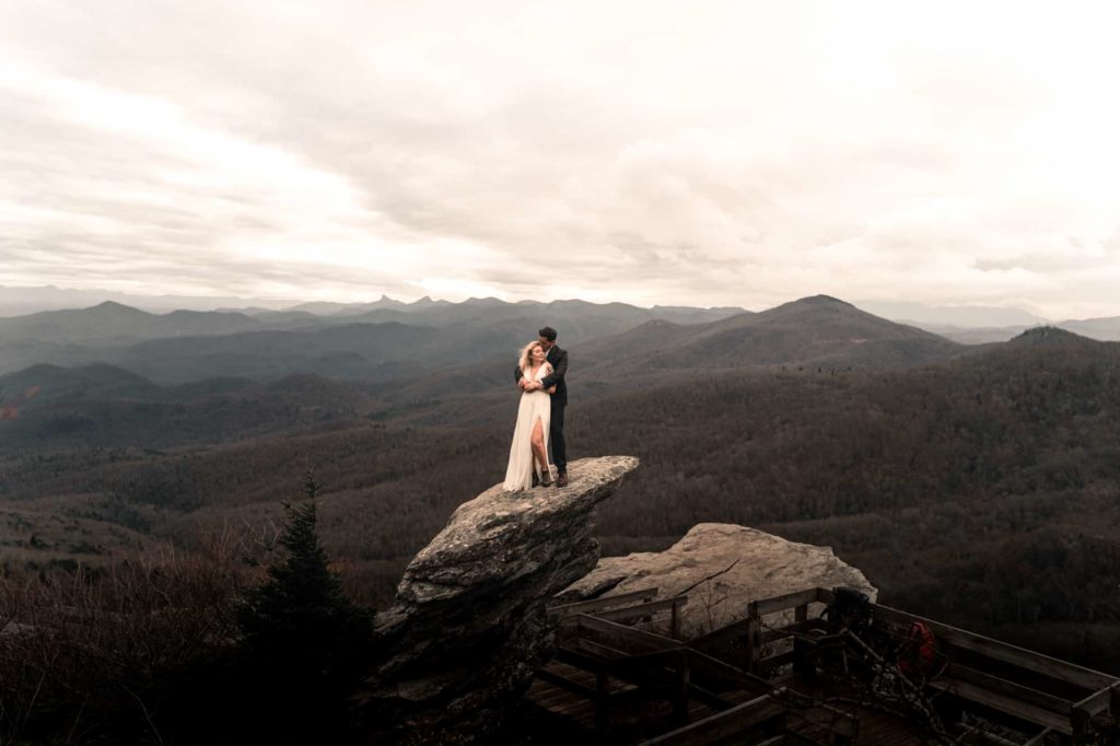 Beautiful photo of Bride and Groom hugging on rock formation with view of hills and mountains