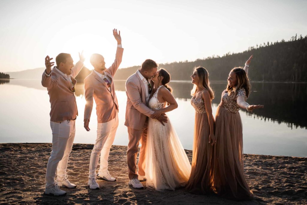 Exciting photo of Groomsmen and Bridesmaids cheering for the newlywed Bride and Groom hugging and kissing