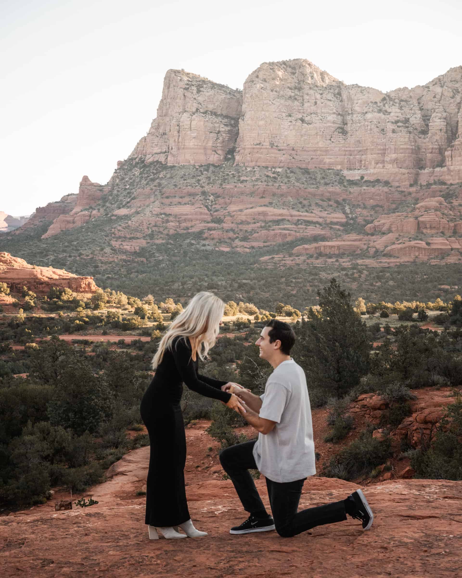 couple proposing to each other, the guy is on his knee and the girl is surprised. there's an epic sedona mountain in the background