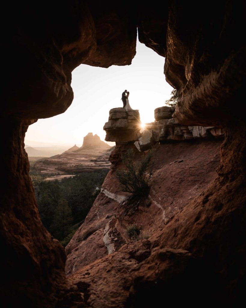 Photo of Bride and Groom kiss captured in Sedona, Arizona, with the couple silhouetted in a cave opening against the setting sun
