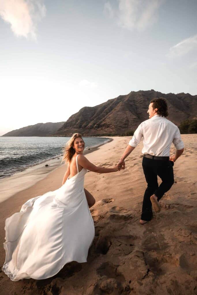 bride and groom running on the beach in hawaii on their destination wedding.