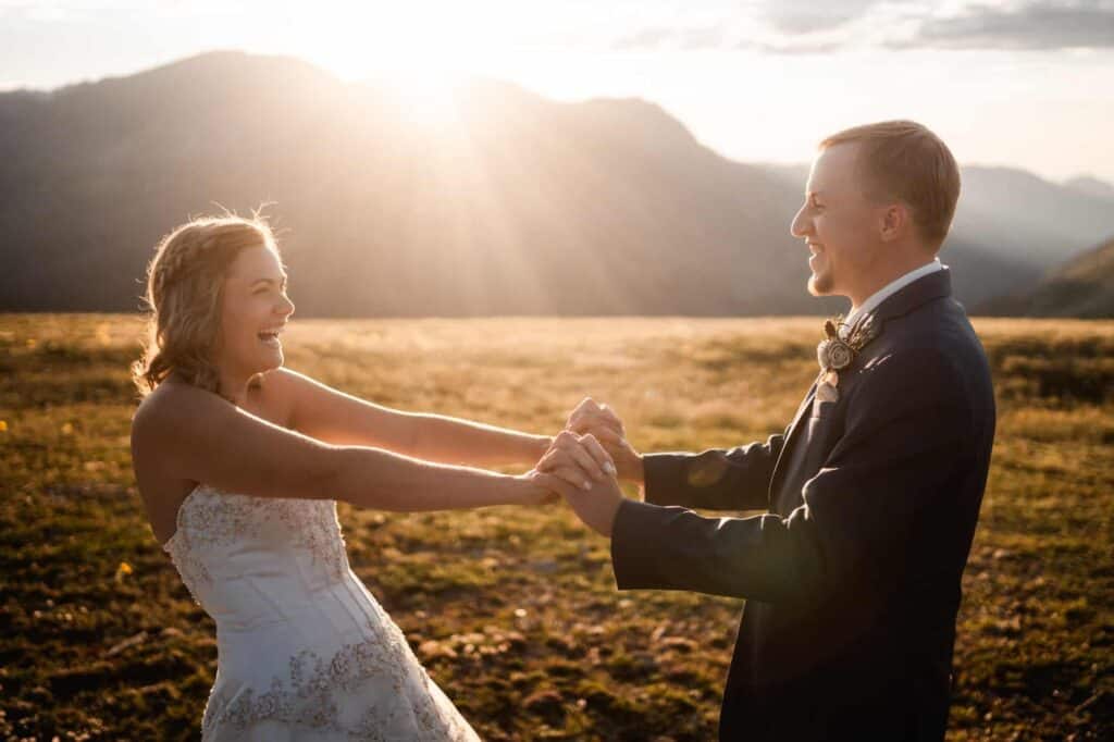 bride and groom holding hand, smiling at each other with epic sunset for their wedding