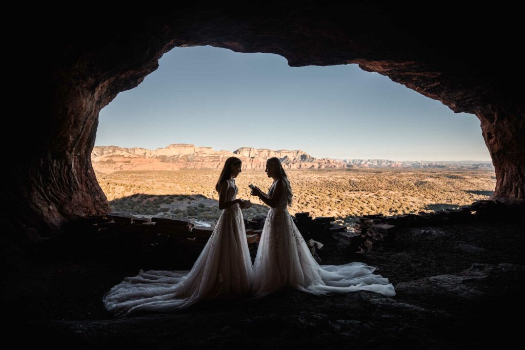 Two brides in elegant dresses during their elopement ceremony in an Arizona cave with a desert backdrop